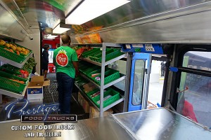 interior of mobile produce truck with shelves full of cartons of vegetables and employee standing in center aisle