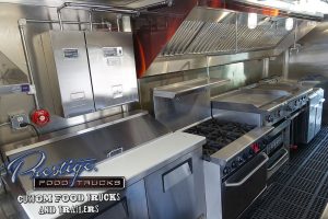 food truck interior showing sandwich prep table, exhaust hood, grill and stove.