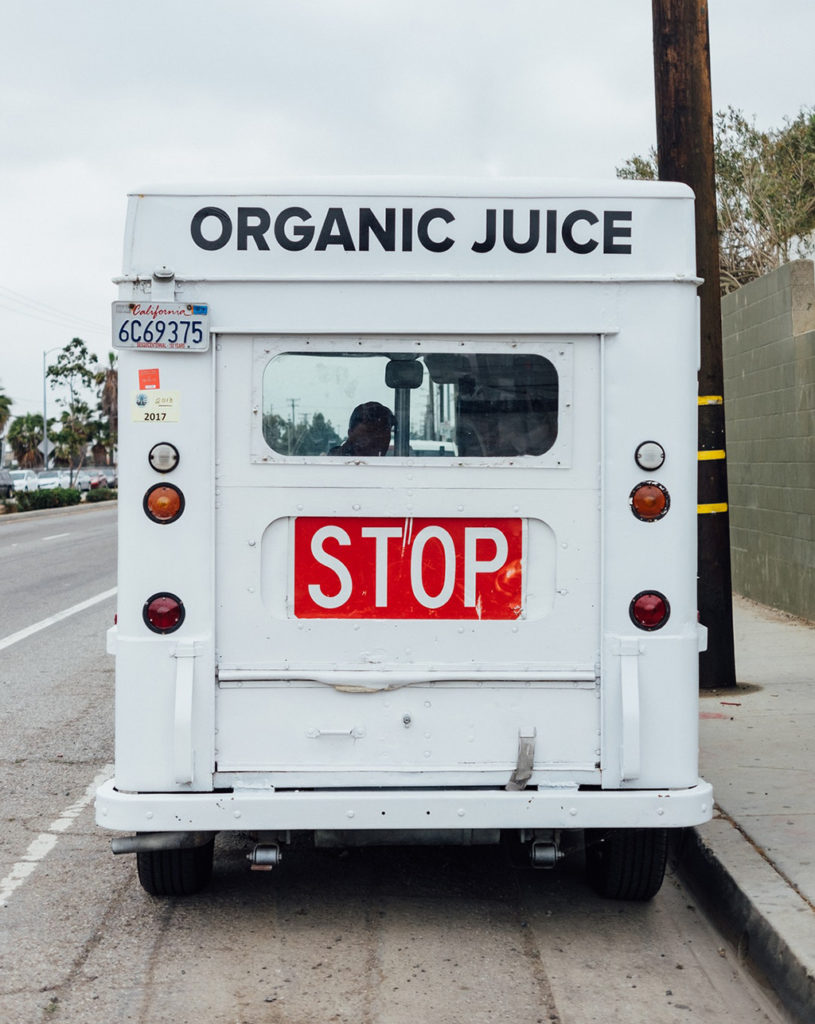 Back of white food truck parked on the side of the road, reads orange juice along the top with a California license plate