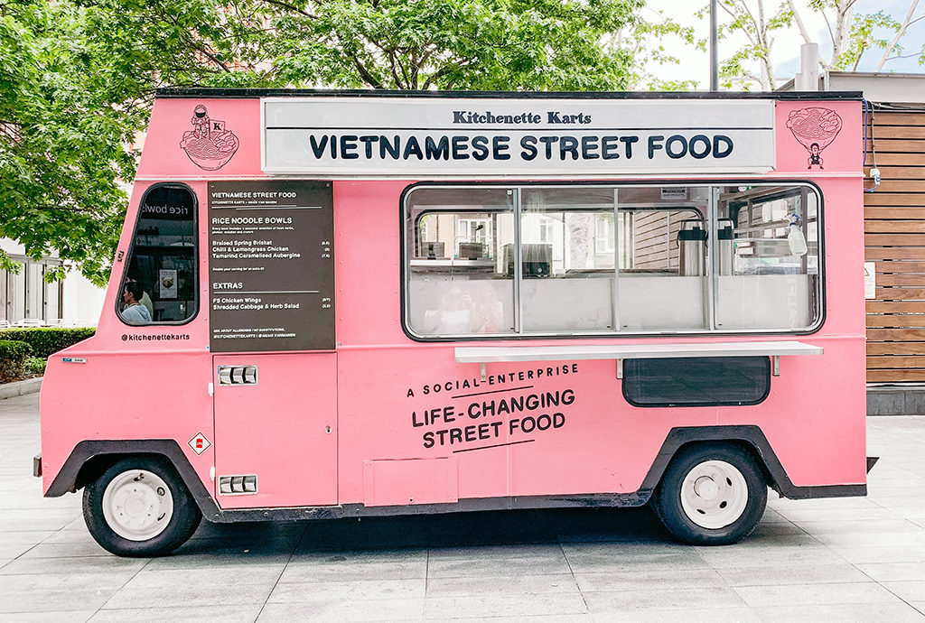 pink food truck selling Vietnamese street food parked on a city plaza