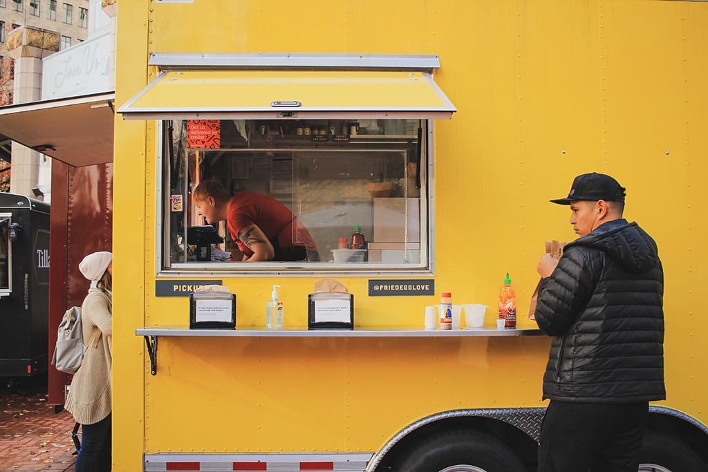 patrons getting food from a yellow food trailer