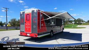 red and gray food truck exterior viewed from rear/side showing side service window, folded out awning and rear door