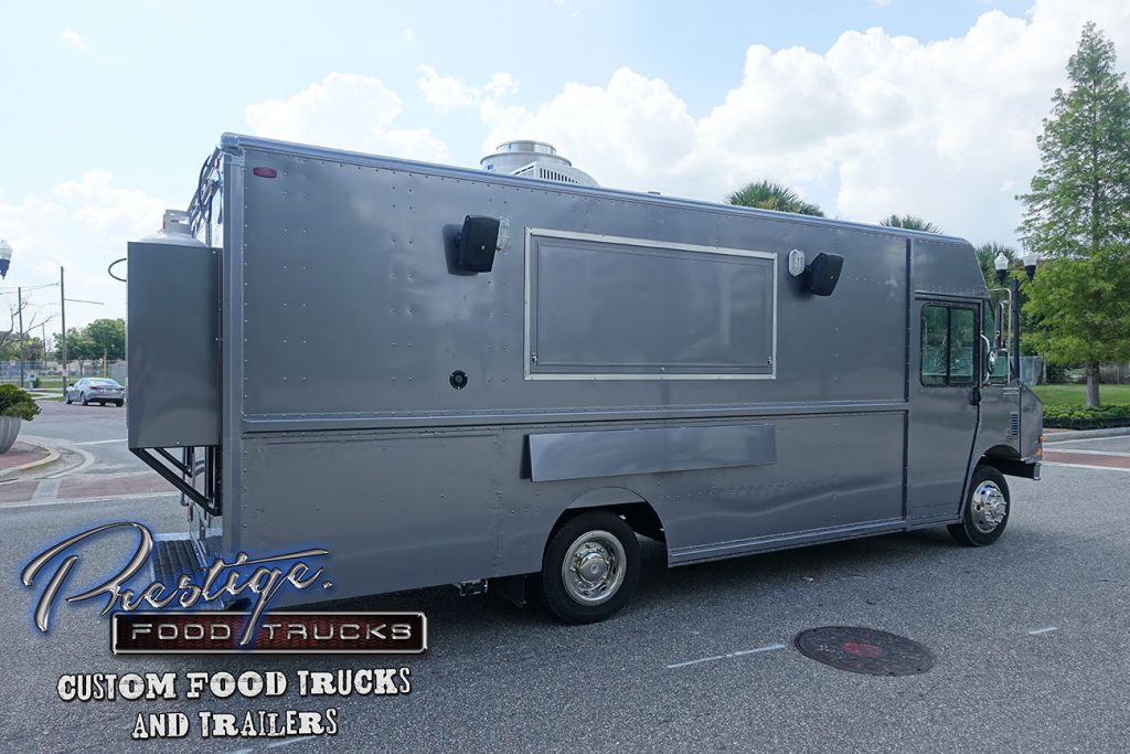 side view of gray food truck with closed service window parked in a parking lot with trees in background
