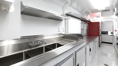 angled photo of one side of a food truck interior with sink, countertop, fridge, and serving window
