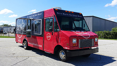 red and black food truck with small serving window parked on asphalt under a blue sky