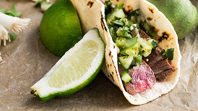 close-up photo of a steak taco with green salsa and limes on the side