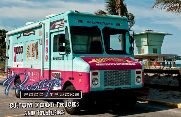 pink and blue food truck parked on the street in a tropical location with palm trees and beach hut in the background