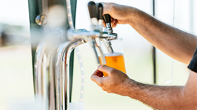 close up photo of man's hands pouring draft beer into a clear cup