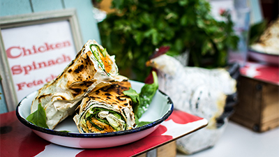 photo of a grilled wrap on a plate on display in front of a sign reading "chicken, spinach, feta cheese"