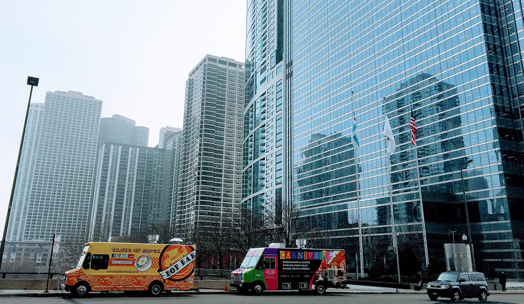 two food trucks parked in front of skyscrapers in a city downtown