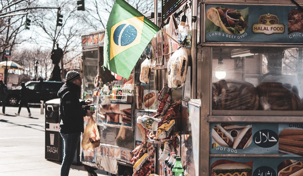 man ordering from food truck selling gyros and hot dogs with Brazilian flag flying