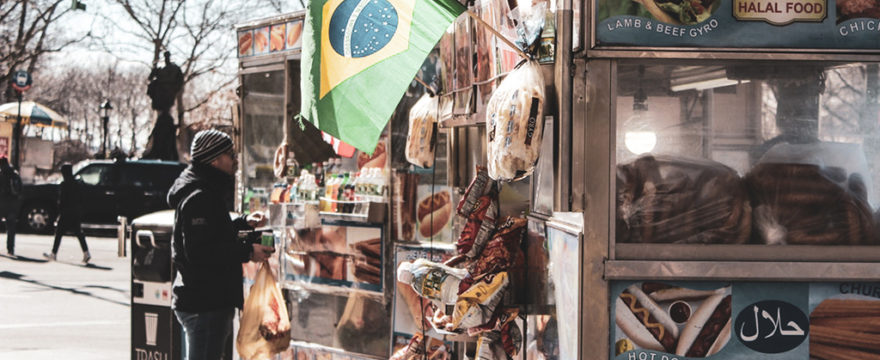 man ordering from food truck selling gyros and hot dogs with Brazilian flag flying