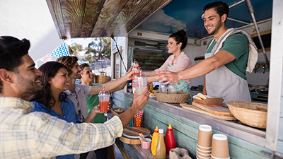 smiling food truck workers serve drinks to a group of young people
