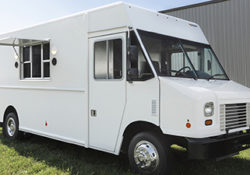 front passenger side photo of a white food truck with it's serving window open and lights on