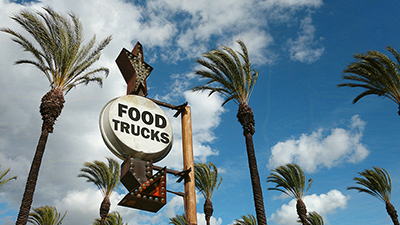 an antique-looking sign surrounded by palm trees that reads "food trucks" with an arrow pointing downward