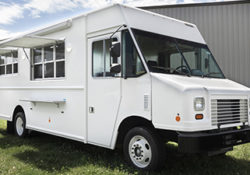 3/4 front angle photo of a white food truck with service windows open parked on grass in front of an industrial building