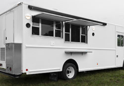photo of a white food truck with two concession windows open in a grassy field on a cloudy day