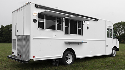 photo of a white food truck with two concession windows open in a grassy field on a cloudy day