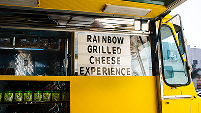 menu window on the side of a yellow food truck reads: rainbow grilled cheese experience