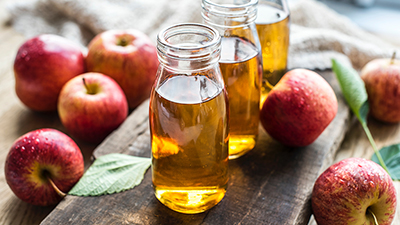 fall themed image with three jars of apple juice on a wooden board surrounded by apples