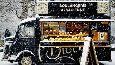 black vintage food truck selling baked goods in a snowy winter scene