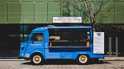 photo of a blue vintage food truck parked in front of urban building on a city street