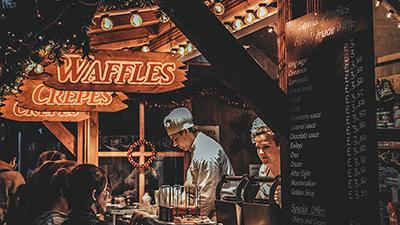 photo of male and female chefs selling from a food stall with signs for waffles and crepes