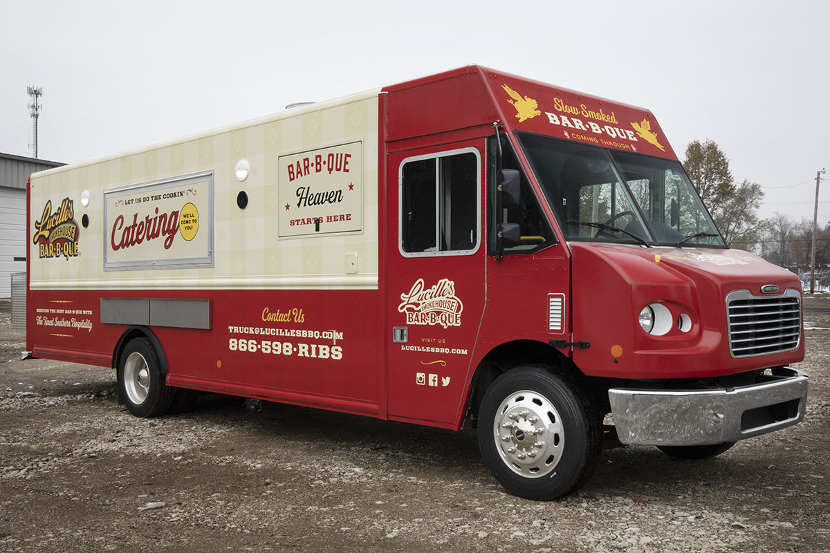 front 3/4 angle photo of a red and cream colored food truck with serving windows closed with exterior lights on