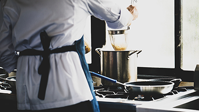 photo of a chef lowering a strainer full of noodles into a pot on a stove