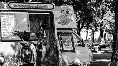 black and white photo of a gelato food truck in a park with customers discussing the menu