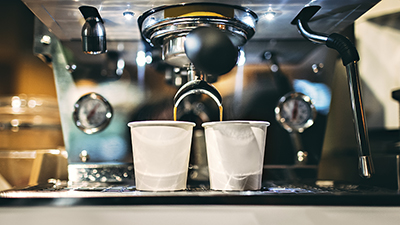 photo of a small espresso machine brewing espresso coffee into two small white cups in a coffee shop