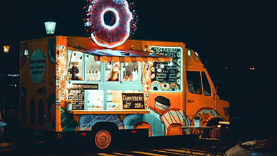 photo of an orange and blue food truck at night time with a neon donut sign