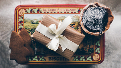 photo of a wrapped gift and cookies on top of a Christmas biscuit tin with snowy background