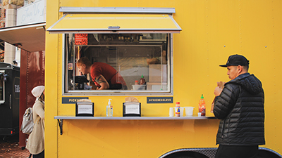 patrons getting food from a yellow food trailer