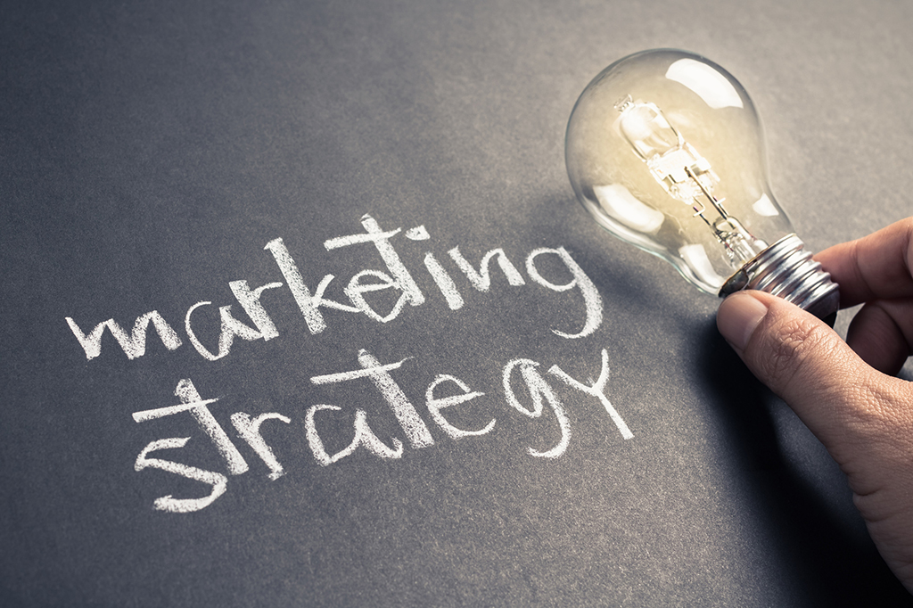 handwritten text that reads "marketing strategy" on chalkboard with glowing light bulb
